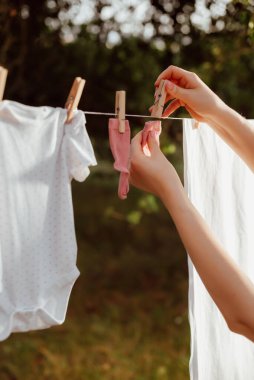 Beyaz elbiseli hamile bir kız bahçeye çocuk iç çamaşırı asıyor.