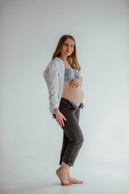 Stüdyoda gri bir duvarın arkasında hamile bir kız var.