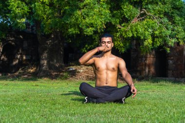 Yoga yapan genç kaslı bir adam ve güneşli bir günde çimenler üzerinde derin meditasyon yapan.