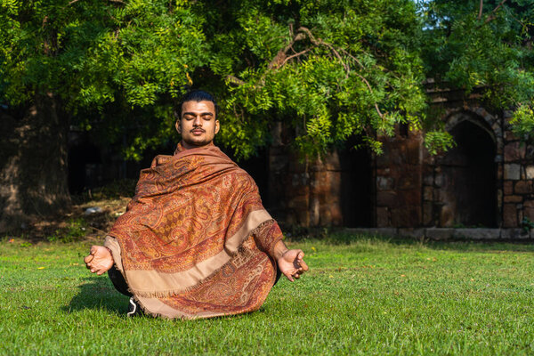 a young muscular man doing yoga and deep meditation on grass while wearing a cap