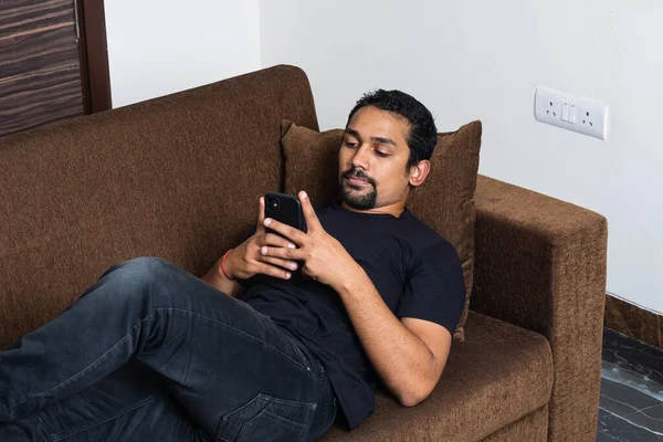 Kanepeye uzanmış siyah elbiseli akıllı telefon kullanan genç bir çocuk.