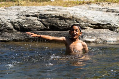 Genç bir köy çocuğu güneşli bir günde suyla dolu nehirde oynuyor.
