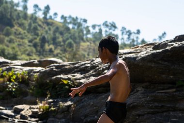 Genç bir köy çocuğu güneşli bir günde suyla dolu nehirde oynuyor.