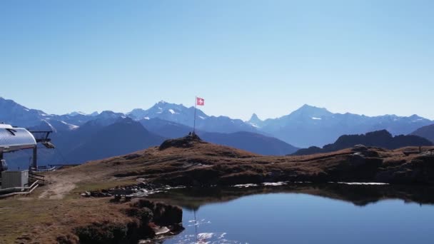 Швейцарський прапор розмахує вітром в ідилічній горі і озерному ландшафті, аеродинамічній орбіті. — стокове відео