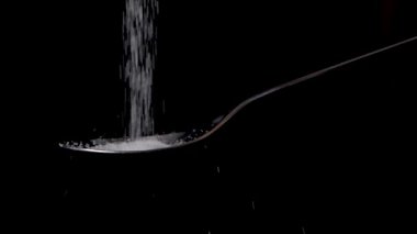 Deniz tuzu dökmek ya da bir kaşığa ağır çekimde siyah arka planda izole etmek.