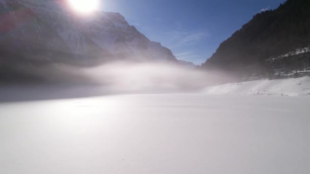 Χαμηλή εναέρια πάνω από χιονισμένη ερημιά και κάτω από λεπτή ομίχλη σε μια σκηνή ηλιοβασιλέματος στο βουνό — Αρχείο Βίντεο