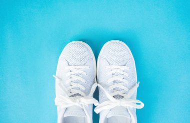 Pair of white female fashion sneakers on blue background.Top view.