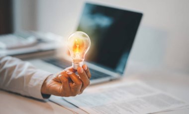 Hand holding light bulb with laptop on wooden desk,Creative new idea,innovation and inspiration.