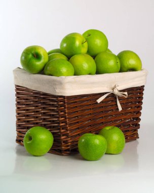 Bir sürü yuvarlak yeşil elma örülmüş kare kahverengi sepet içinde iç keten çantalı ve fiyonklu.