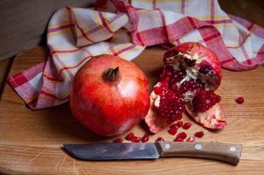Olgun kırmızı nar ve çatlamış nar bileşimi. Ahşap bir arka planda klasik bıçakla. Yakut tohumlarının yakın görüntüsü nar meyvesi
