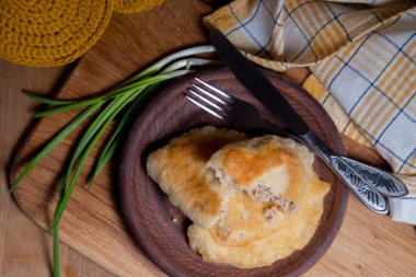 Ahşap masada iki ayrı kızarmış etli kil tabak. Fast food yemeğinin kompozisyonu. İçinde domuz pastası, çatal bıçak ve eski ahşap arka planda yeşil soğan olan iki turta..