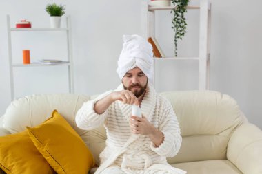 Havlu ve bornozla elinde krem losyon tutan yakışıklı bir adamın güzel portresi. Erkek konsepti için kaplıca, vücut ve cilt bakımı