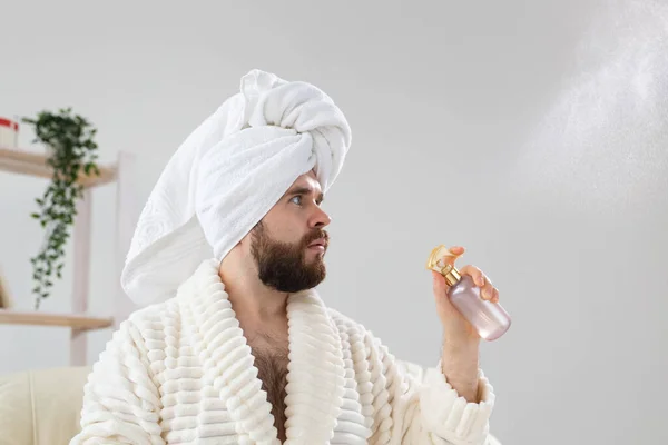 Homem barbudo com toalha de banho na cabeça aplicando tratamento de água spray no rosto. Spa, corpo e cuidados com a pele para o conceito de homem. — Fotografia de Stock