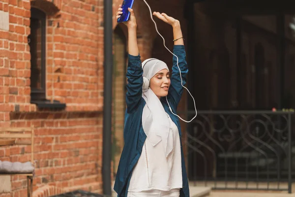 Nahöstliche Frau im Hidschab hört Musik mit Kopfhörern und tanzt im Freien. Frauenunabhängigkeit und Feminismus-Konzept. — Stockfoto