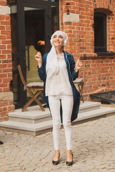 Mellanösterns kvinna i hijab lyssnar musik med hörlurar och dansar utomhus. Kvinnors oberoende och feminism. — Stockfoto