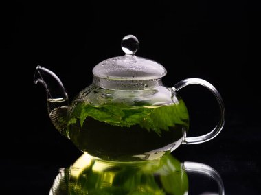 Siyah arka planda sıcak cam çaydanlık, yeşil nane çayı. Bitki çayı ve sağlıklı içecek konsepti.