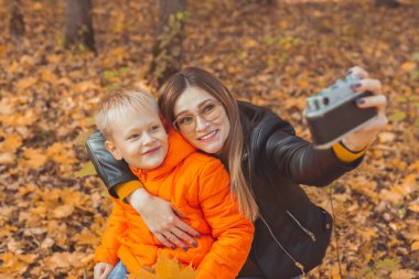 Oğlu ve annesi sonbahar parkında selfie çekiyorlar. Bekar ebeveyn, boş zaman ve sonbahar konsepti.