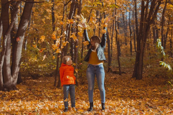 Single parent family playing with autumn leaves in park. Happy mom and son throw autumn leaves up in fall park. — Stock Photo, Image