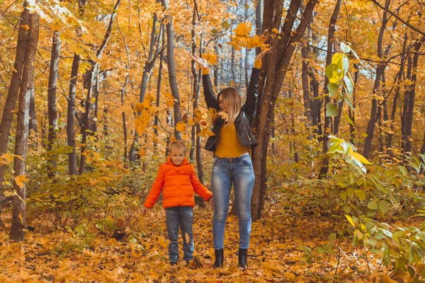 Ensamstående föräldrar leker med höstlöv i parken. Lycklig mamma och son kastar höstlöv upp i höstparken. — Stockfoto