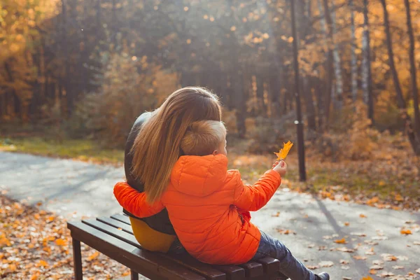 Madre soltera y niño en el otoño en el parque se sientan en el banco. Temporada de otoño y concepto familiar. —  Fotos de Stock