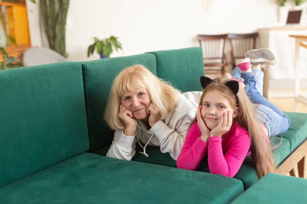 Nieta feliz y abuela tumbada en un sofá en pose divertida. La abuela se divierte con su nieto en casa. Concepto de personas mayores, familia y generación. —  Fotos de Stock