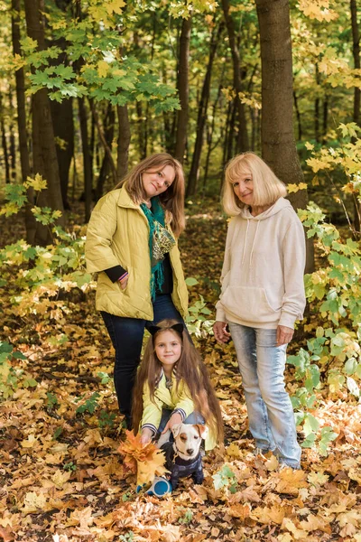 Portrét tří generací šťastné krásné ženy a psa dívající se do kamery, objímající a usmívající se v podzimní přírodě. — Stock fotografie