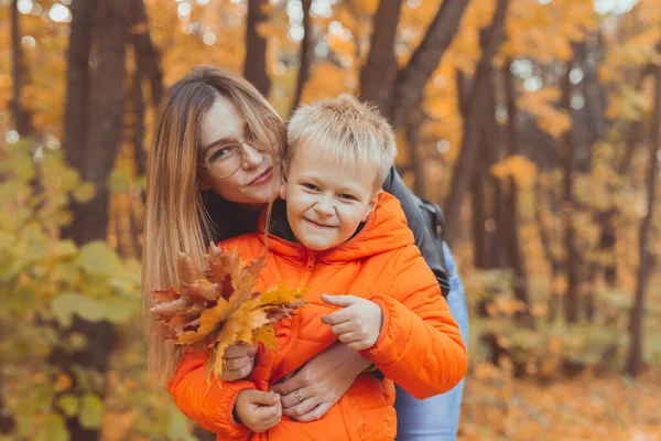 Madre abrazando a su hijo durante el paseo en el parque de otoño. Temporada de otoño y concepto de padre único. —  Fotos de Stock