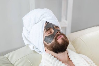 Sakallı adamın cildi temiz, yüzüne kil maske takıyor ve güzellik tedavisinden hoşlanıyor. Evde spa, vücut ve cilt bakımı