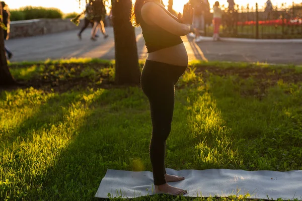 黒いスーツの赤ちゃんを期待している若い女性の側のビューのクローズアップは、ラグ裸足で立ち、暖かい晴れた夏の日に瞑想します。スポーツと瞑想活動の概念 — ストック写真