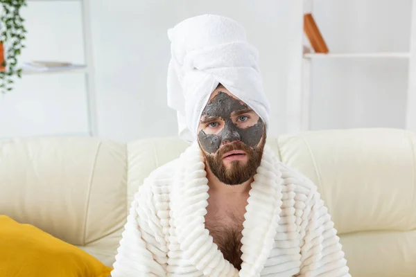 El hombre barbudo tiene la piel limpia y fresca, lleva máscara de arcilla de belleza en la cara y disfruta de tratamientos de belleza. Spa en casa, cuidado corporal y de la piel —  Fotos de Stock