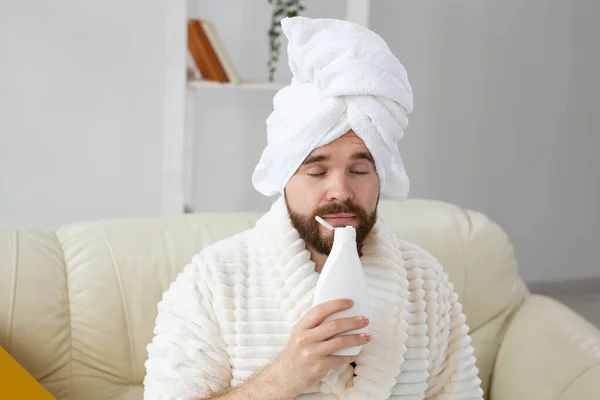 Бородатый мужчина с полотенцем на голове и кремом для тела. Парень улыбается, когда чувствует запах крема на руке. Спа, уход за телом и кожей для человека — стоковое фото