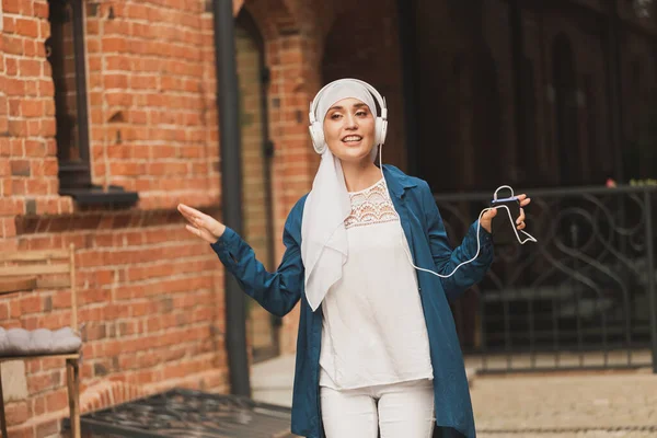히잡을 입은 중동 여성 이 헤드폰으로 음악을 듣고 밖에서 춤을 추고 있습니다. 여성의 독립 과 여성주의 개념. — 스톡 사진