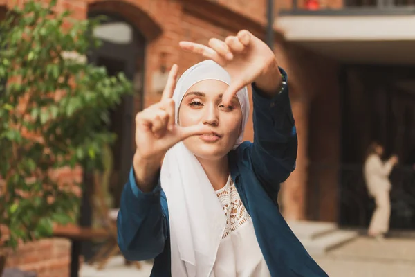 Retrato de menina muçulmana jovem fazendo uma moldura de câmera com os dedos ao ar livre. — Fotografia de Stock