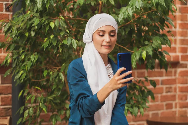 Mulher jovem muçulmana usando lenço de cabeça hijab na cidade mensagens de texto telefone celular — Fotografia de Stock