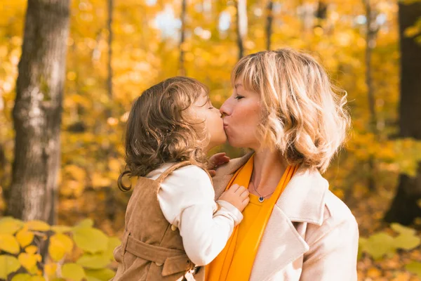 Женщина с девочкой на улице осенью. Ребенок целует маму. День матери праздник и осенняя концепция. — стоковое фото