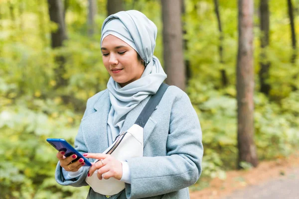 Mulher muçulmana no parque usando smartphone conectado on-line sem fio — Fotografia de Stock