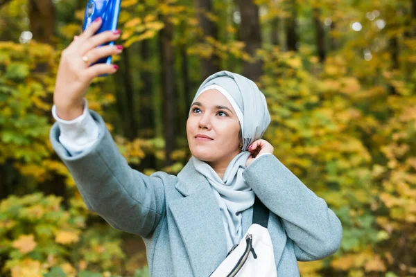 Genç Arap Müslüman kadın tesettüre girmiş, parkta cep telefonuyla selfie çekiyor. İnsanlar dini yaşam tarzı konsepti. — Stok fotoğraf
