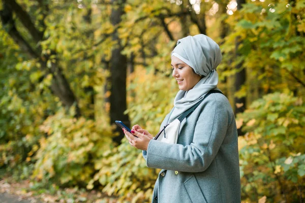 Parktaki Müslüman kadın internete bağlı akıllı telefon kullanıyor. Reklam için alan — Stok fotoğraf