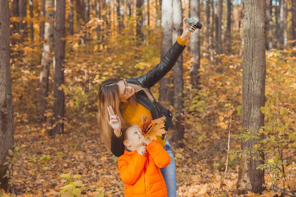 儿子和母亲正在秋天公园的摄像机前自拍。单亲、闲暇和秋天的概念. — 图库照片
