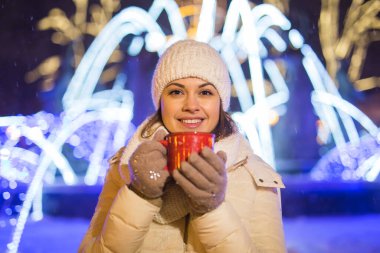 Kış boyunca ayakta duran kız. Arka planda kar yağıyordu. Sıcak ceket şapkası takıyor, çay ve sıcak çay içiyordu..
