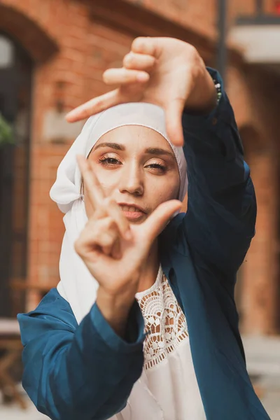 Porträtt av ung muslimsk flicka som gör en kameraram med fingrar utomhus. — Stockfoto