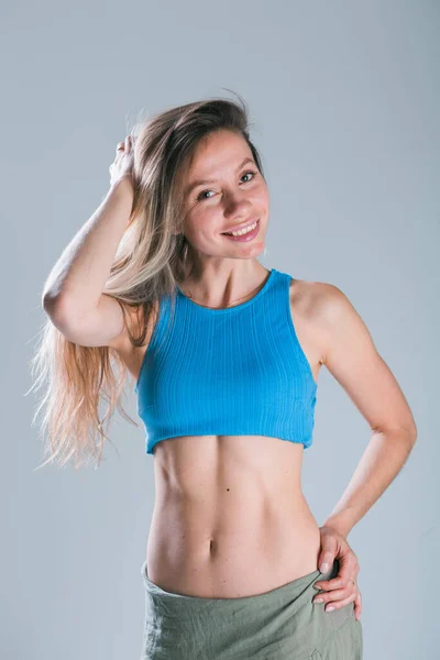 Koncepcja sprawności i diety. Portret młodej kobiety z idealnym ciałem sportowym i ładnym płaskim brzuchem w seksownej bluzce sportowej na szarym tle. — Zdjęcie stockowe