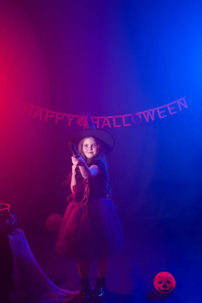 Kleines Mädchen hält Besen im Halloween-Urlaub. Mädchen tragen Hexenkostüm. Fantasie, Märchen und Maskerade-Konzept. — Stockfoto