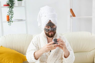 Sakallı adamın cildi temiz, yüzüne kil maske takıyor ve güzellik tedavisinden hoşlanıyor. Evde spa, vücut ve cilt bakımı