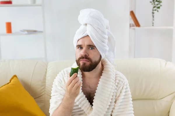 面白い髭の男がキュウリのスライスを顔に持っている。自宅でスパ,男性のコンセプトのためのボディ&スキンケア. — ストック写真