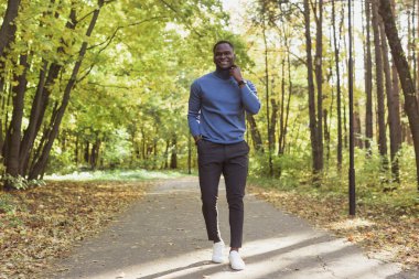 Afrikalı Amerikalı öğrenci sonbahar sezonunda parkta yürüyor.
