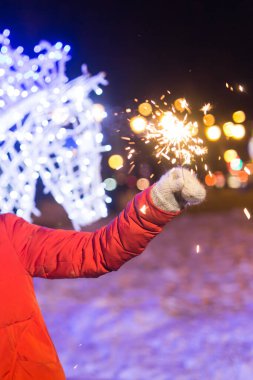 Örgü şapkalı ve atkılı kadın Bengal ışığı ve maytapla şehirde dikiliyor. Kutlama ve Noel kavramı.