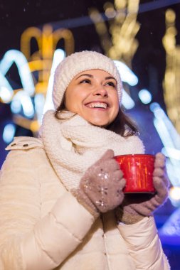 Kış boyunca ayakta duran kız. Arka planda kar yağıyordu. Sıcak ceket şapkası takıyor, çay ve sıcak çay içiyordu..