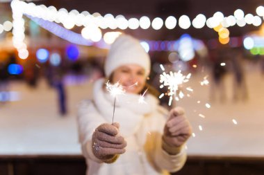 Örgü şapkalı ve atkılı genç bir kadın Bengal ışığı ve maytapla şehirde dikiliyor. Kutlama ve Noel kavramı.