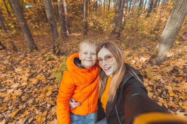 Hijo y madre se están tomando selfie en cámara en el parque de otoño. Concepto de temporada monoparental, de ocio y otoño. —  Fotos de Stock